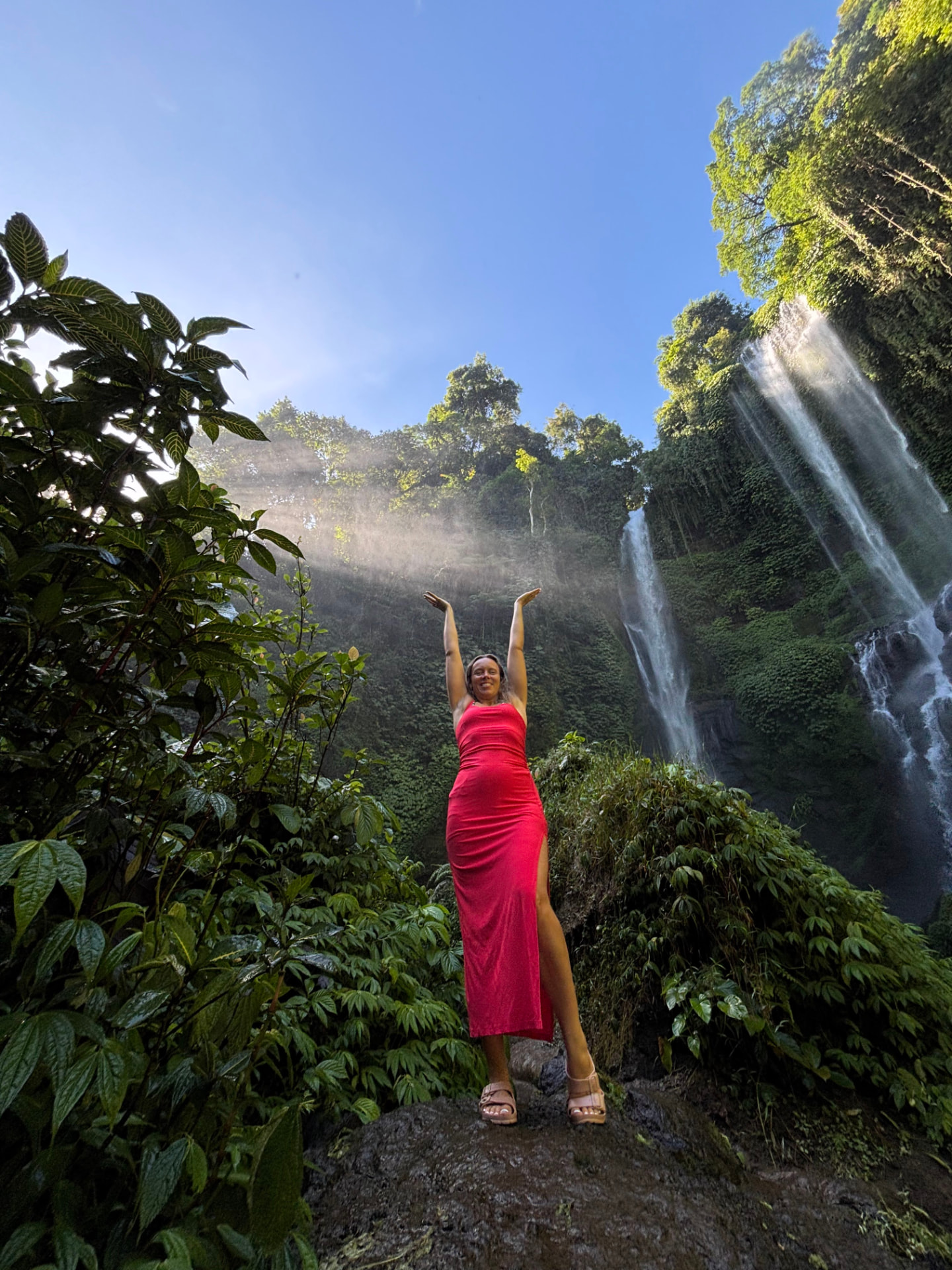 Mulher de braços erguidos perante uma cascata